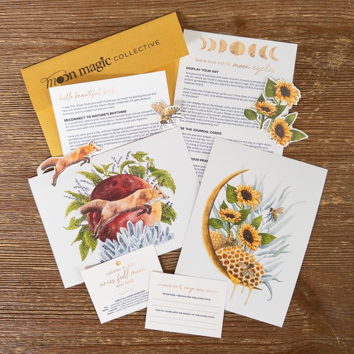 A flat lay of printed journaling and affirmation cards, stickers, and a gold envelope on a wooden surface. The cards feature watercolor illustrations of foxes, sunflowers, honeycombs, and moon phases, with gold foil text and decorative elements.